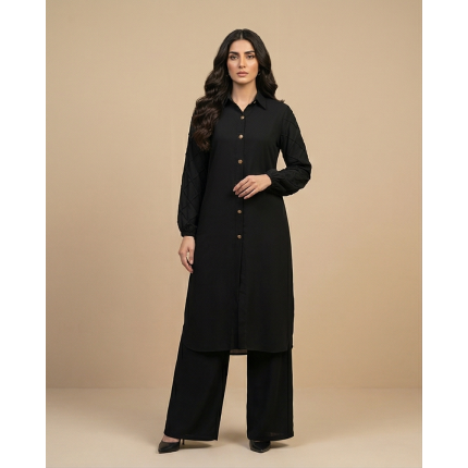 Woman walking in a minimalist corridor wearing a black sheesha georgette co-ord set with a long tunic and wide-leg trousers.