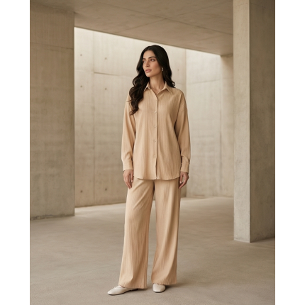 Woman standing in a minimalist white setting wearing a crisp ivory Irish linen co-ord set with a button-down shirt and matching wide-leg pants.