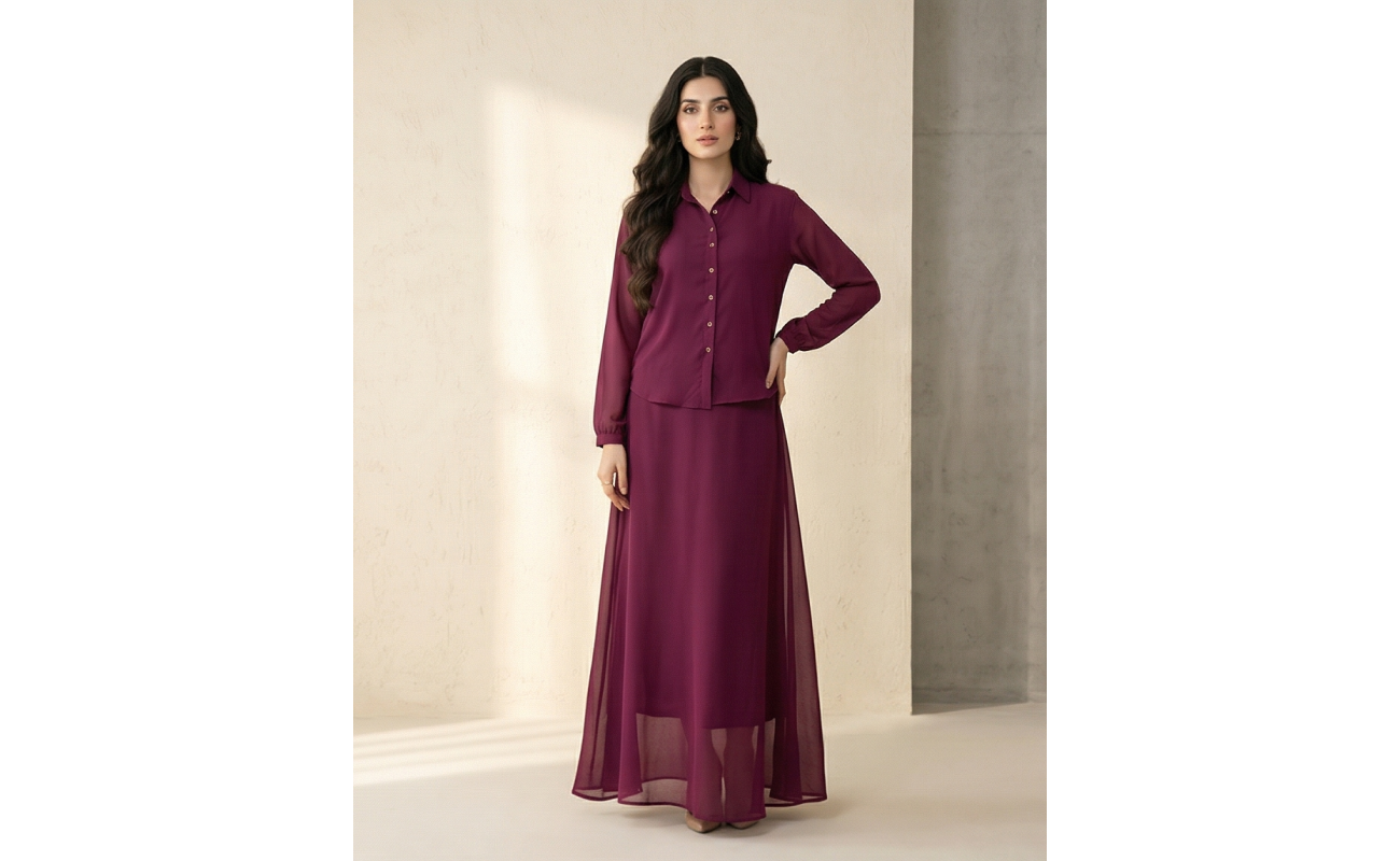 A tall woman standing against a neutral wall wearing a deep wine-colored Mulberry Georgette Maxi dress with a button-up collar and long sleeves.