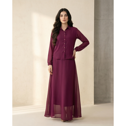 A tall woman standing against a neutral wall wearing a deep wine-colored Mulberry Georgette Maxi dress with a button-up collar and long sleeves.